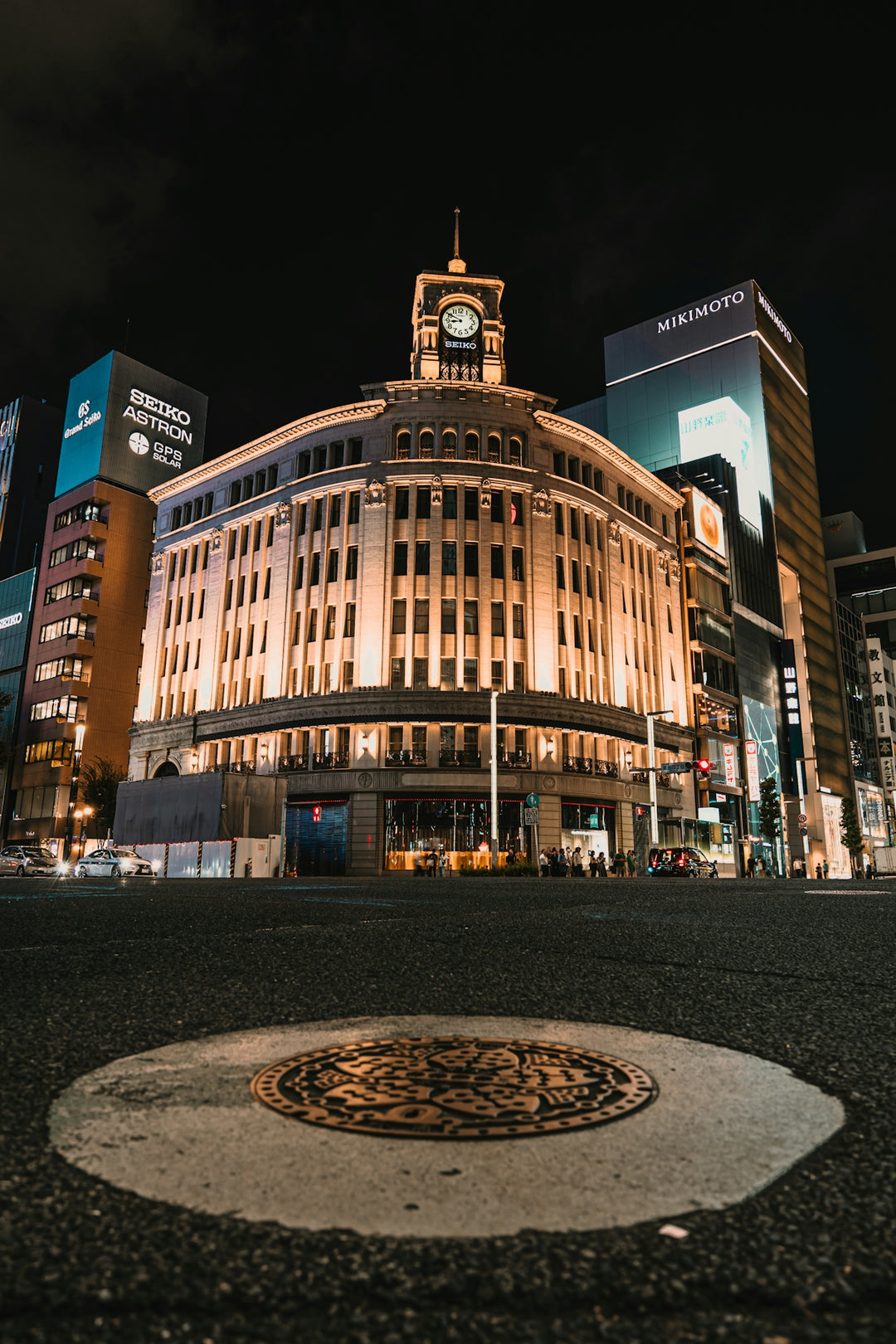 Illuminated building at night with a manhole cover foreground.