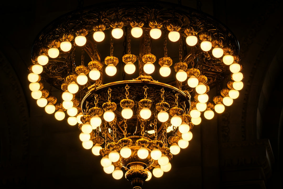 A large tiered brass chandelier with glowing round bulbs in a dark room